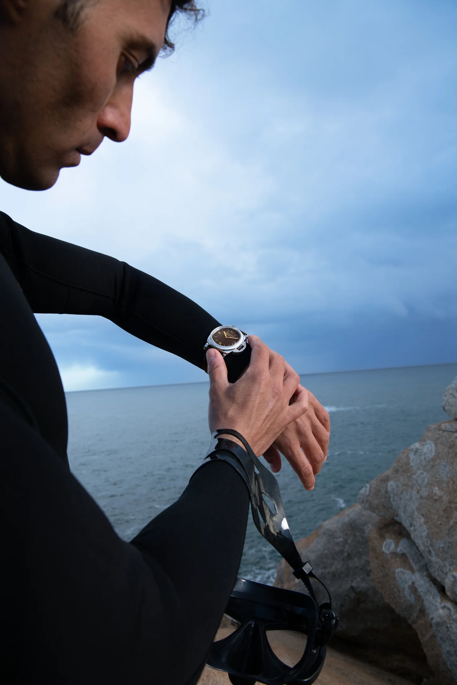 Diver checking a Panerai watch on the rocky coast.
