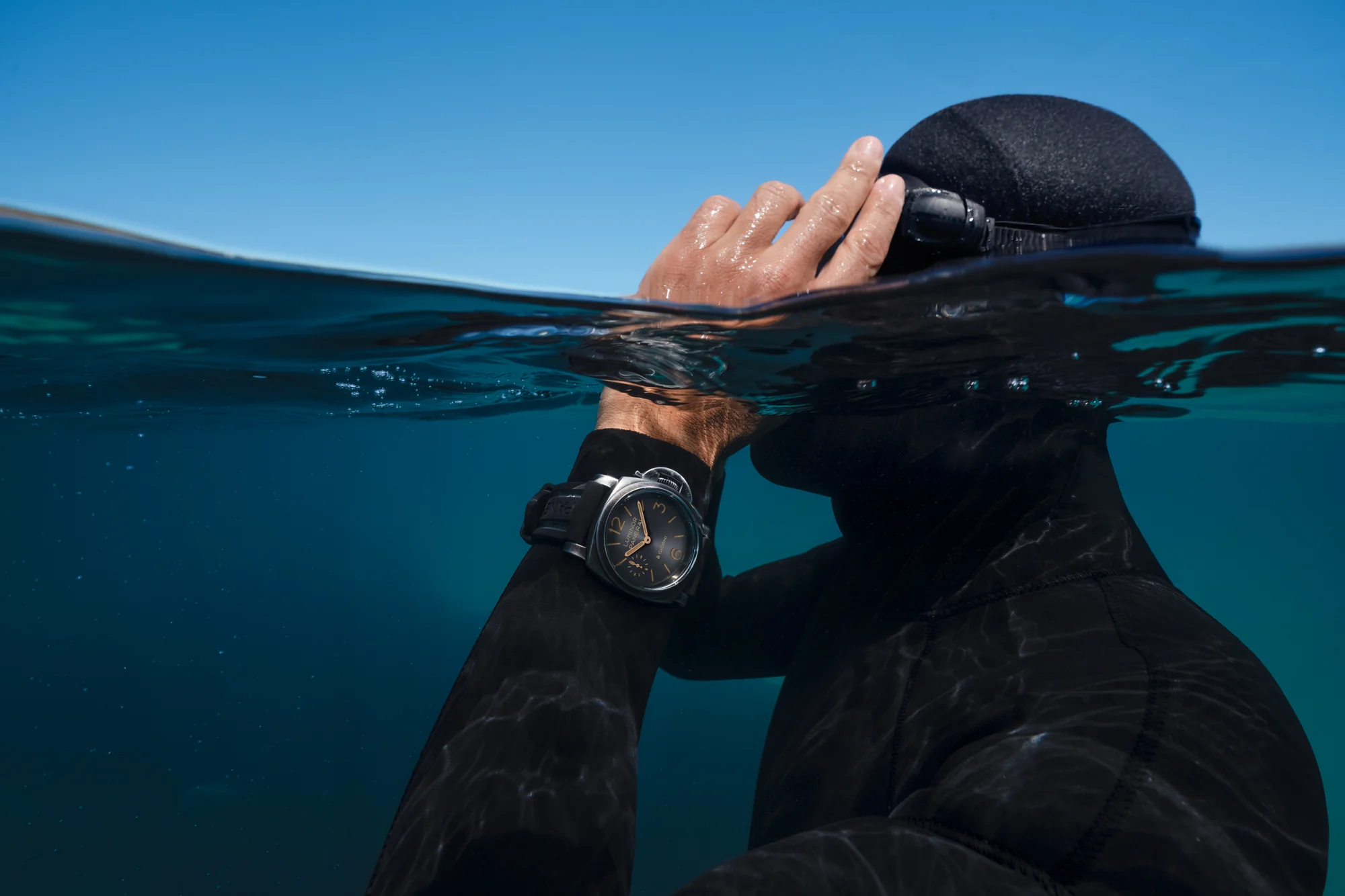 Diver adjusting a mask at the waterline, wearing a Panerai watch.
