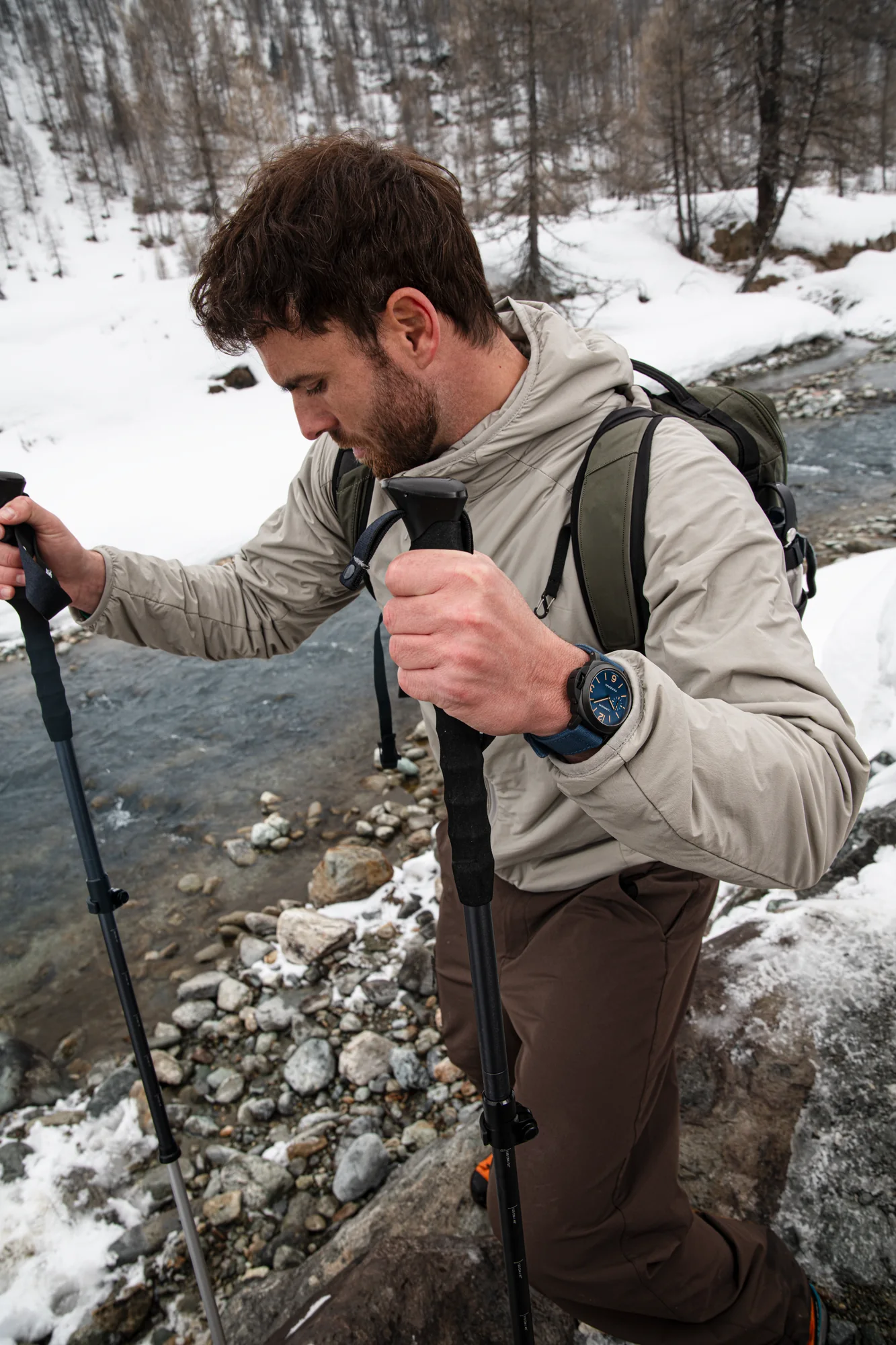 Mountain explorer crossing a snowy stream with a Panerai watch